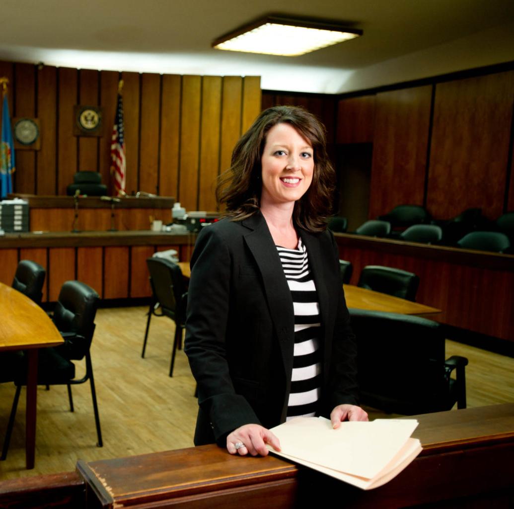 A female dressed professionally standing in a court room smiling at the camera. 