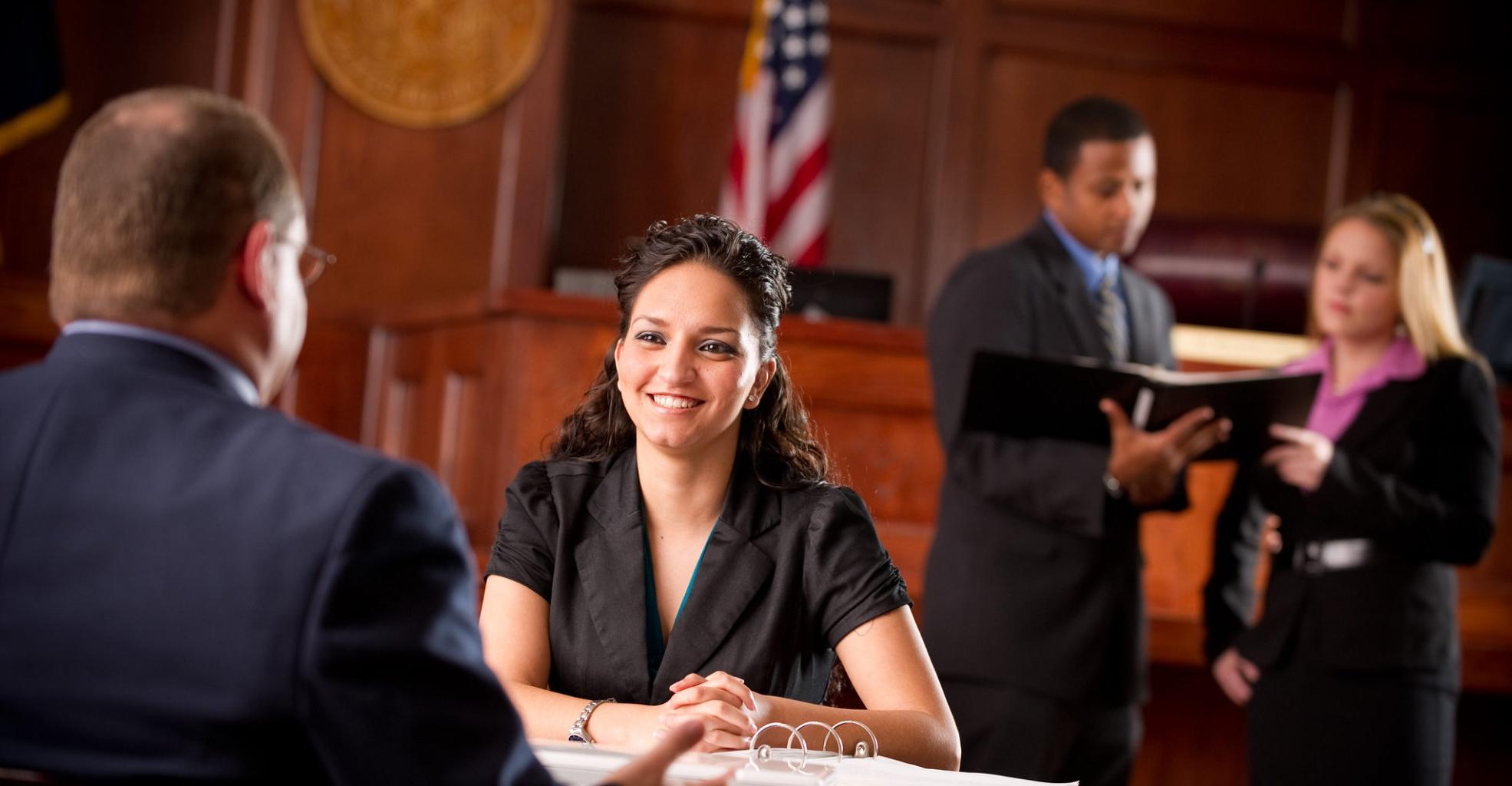 Woman approaching judges desk with individual discussing a case in the background.
